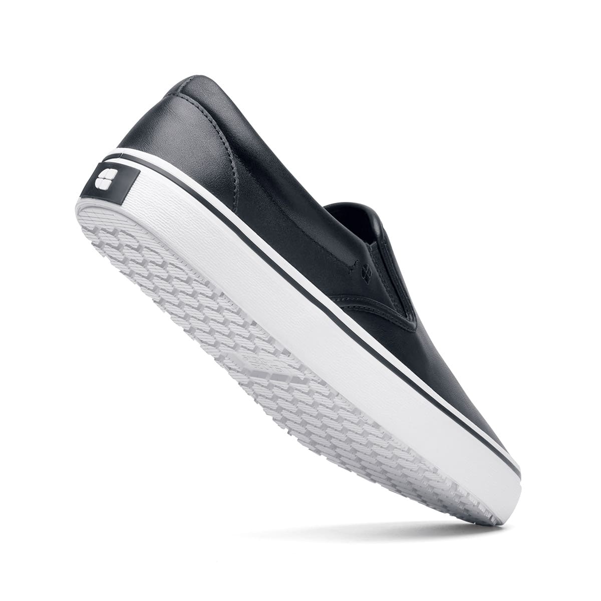 The Merlin Slip On Black and White from Shoes For Crews are slip-on trainers that are slip-resistant, lightweight, easy to clean and water-resistant, seen from the perpendicular.